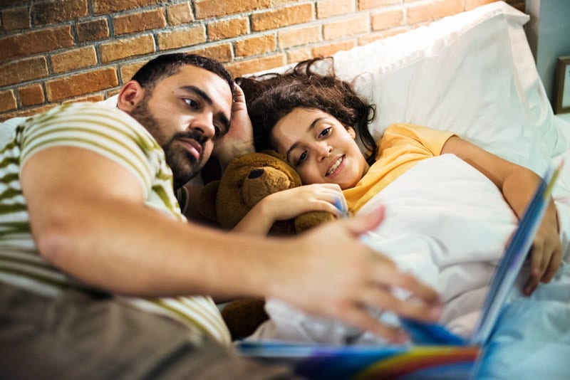 hispanic father and child reading in bed