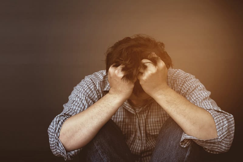 man hunched over with arms on knees and hands in hair