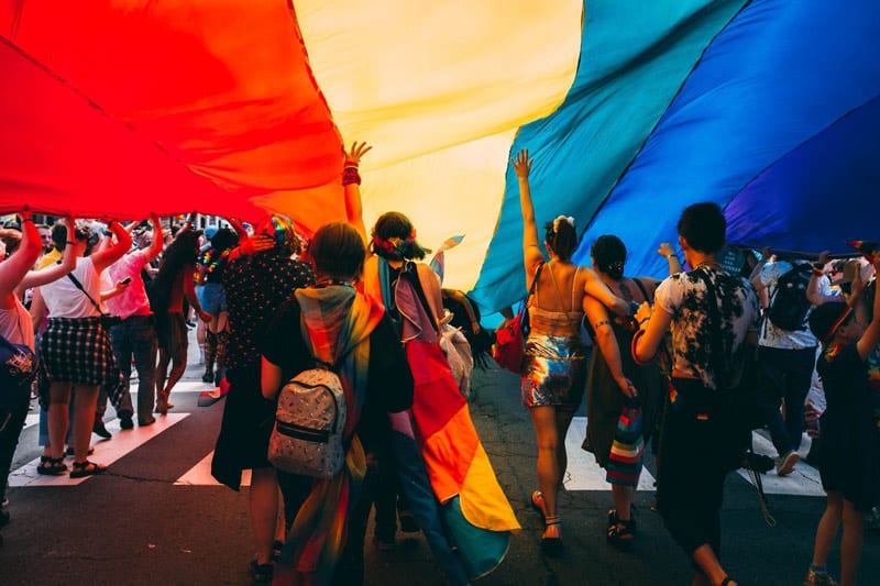 group of people walking under pride flag