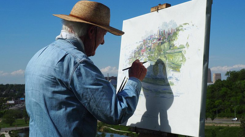 man in hat painiting outdoors