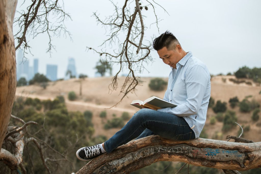 man reading book on tree limb