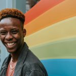 smiling man in front of Pride colors