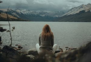 teen sitting before mountain lake