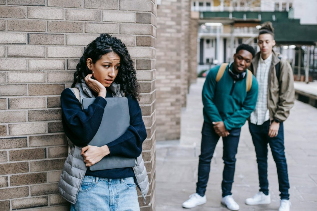 Female student hiding around the corner from two male students