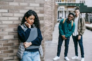 Female student hiding around the corner from two male students
