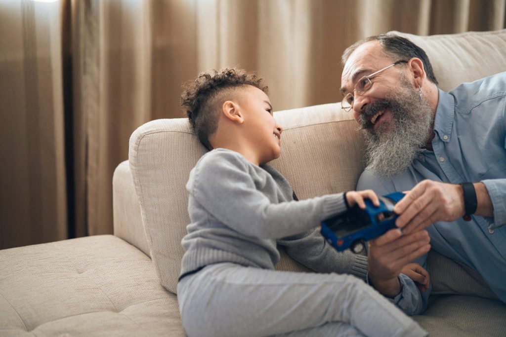 Older bearded man playing with grandson at home