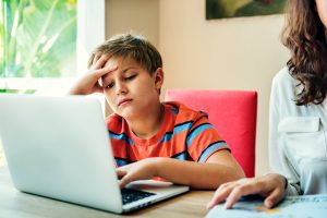 Young boy doing homework on laptop with his mother