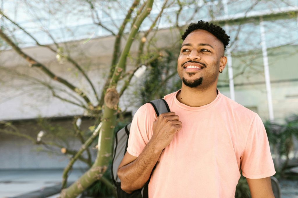 Smiling man in pink T-shirt carrying a backpack.