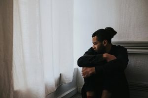 Man sitting on the floor by a window, looking pensive and reflective, symbolizing an emotional struggle
