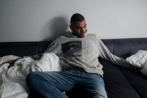 Worried man in sweatshirt and jeans sitting on couch