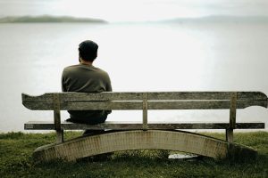 Person sitting alone on a weathered bench overlooking a calm lake, symbolizing reflection and emotional exploration.