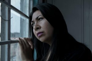 woman gazing out the window into a gloomy sky