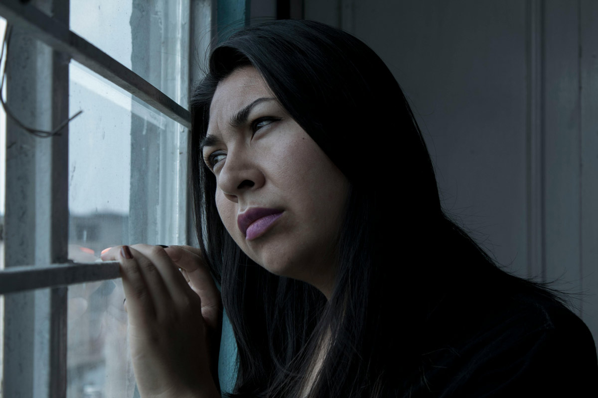 woman gazing out the window into a gloomy sky