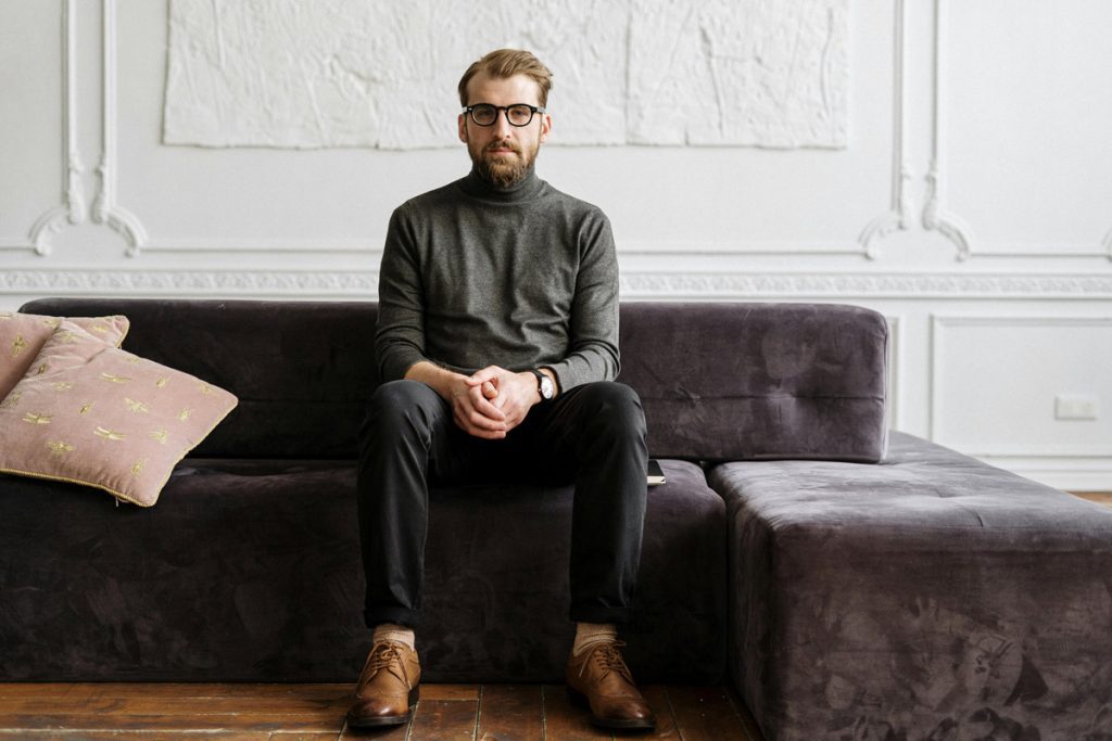 Bearded man with glasses sitting on purple couch