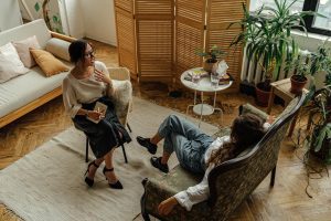 Female therapist sitting in a chair across from a female client sitting on a couch.