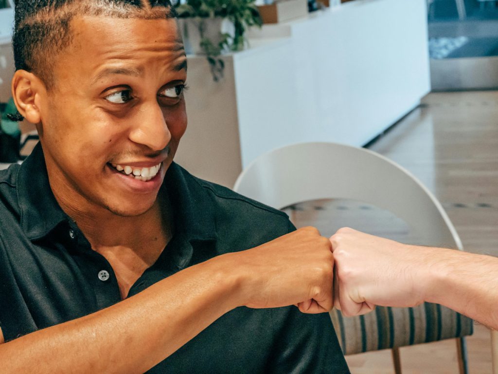 A happy man shares a fist bump with a friend.