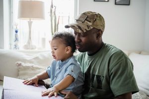 Father and child sitting together and holding a coloring book, symbolizing family support during a veteran's recovery journey.