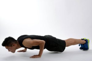 Lean and muscular young man doing push-ups on a white floor.