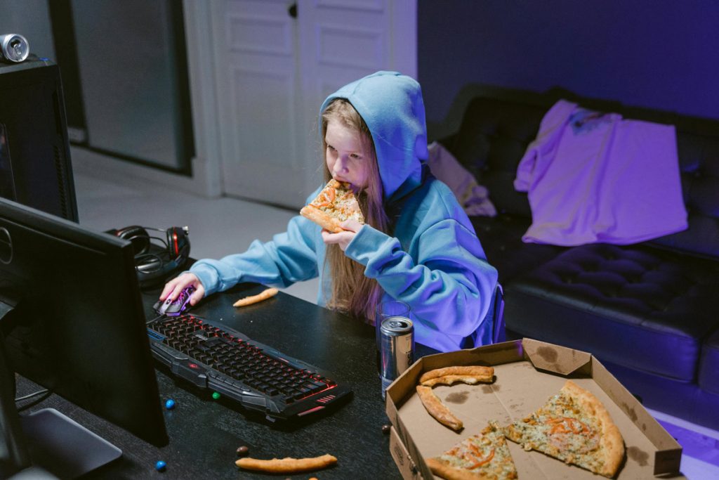 Teen girl playing a computer game while eating pizza, representing how food and other habits can become coping strategies for emotional neglect.
