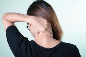 Young woman rubbing a sore neck from behind.