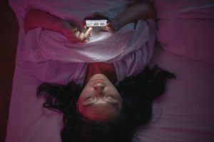 Woman lying in bed anxiously looking at her smartphone, representing late-night health symptom searching and health anxiety.