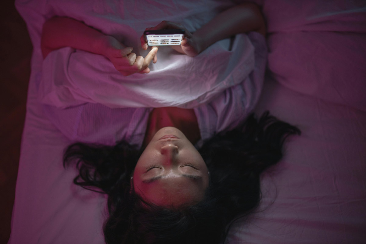 Woman lying in bed anxiously looking at her smartphone, representing late-night health symptom searching and health anxiety.