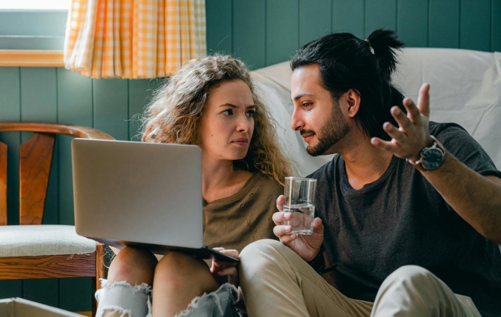 "Man and woman sitting on floor with laptop considering mental health therapy choices."