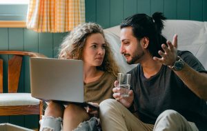 "Man and woman sitting on floor with laptop considering mental health therapy choices."