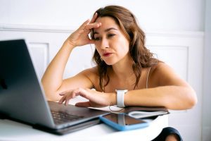 Woman looking tired and contemplative while looking at laptop, hand on forehead