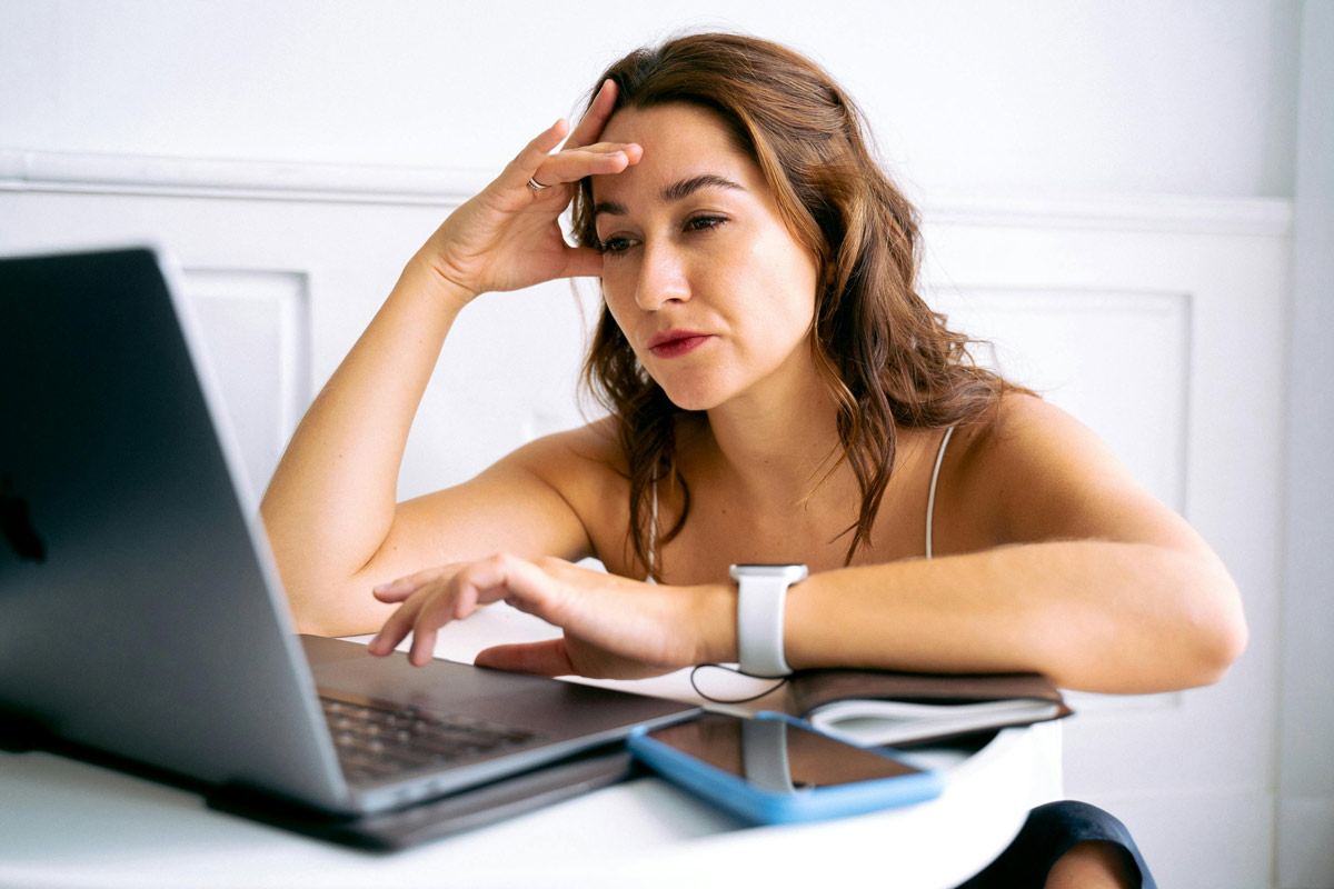 Woman looking tired and contemplative while looking at laptop, hand on forehead