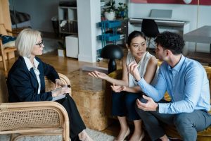 Couple sitting on couch during marriage counseling session with therapist in background.