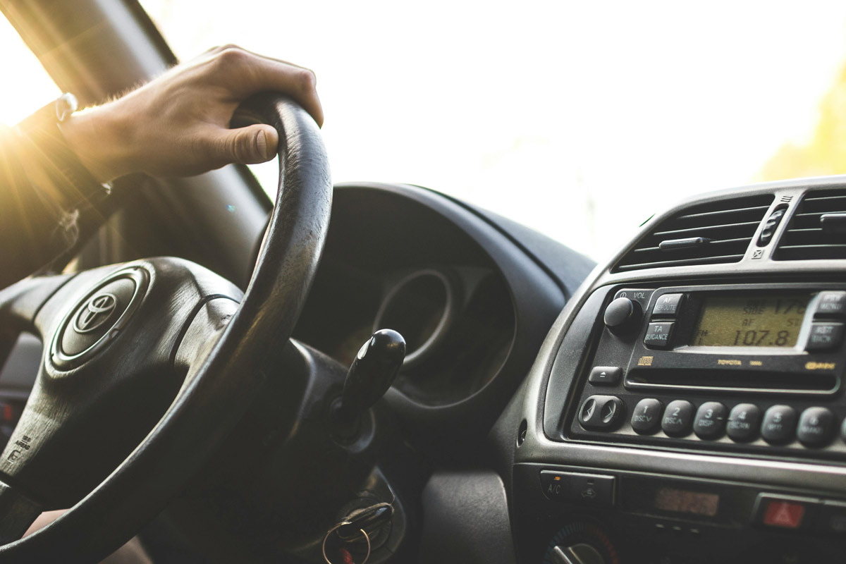 Person's hand on steering wheel of car with sunlight streaming through windshield, representing driving anxiety and OCD recovery journey.