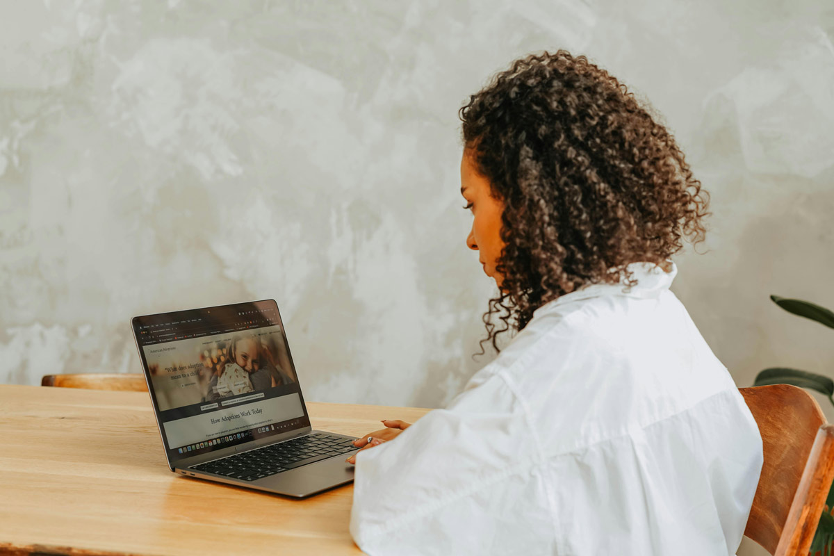 Woman with curly hair sitting at table looking at laptop screen while searching for a marriage and family therapist online.