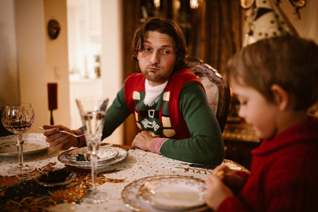 Tired man looking at child during holiday meal, representing stress and mental health during the holidays.