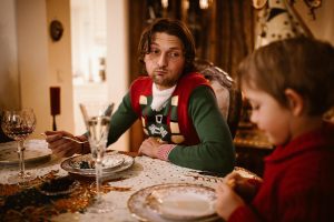 Tired man looking at child during holiday meal, representing stress and mental health during the holidays.