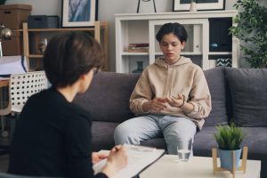 Teen in hoodie sitting on couch speaking with a psychiatrist.