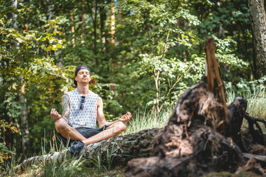 Man meditating peacefully on a log in nature during a mental health retreat.