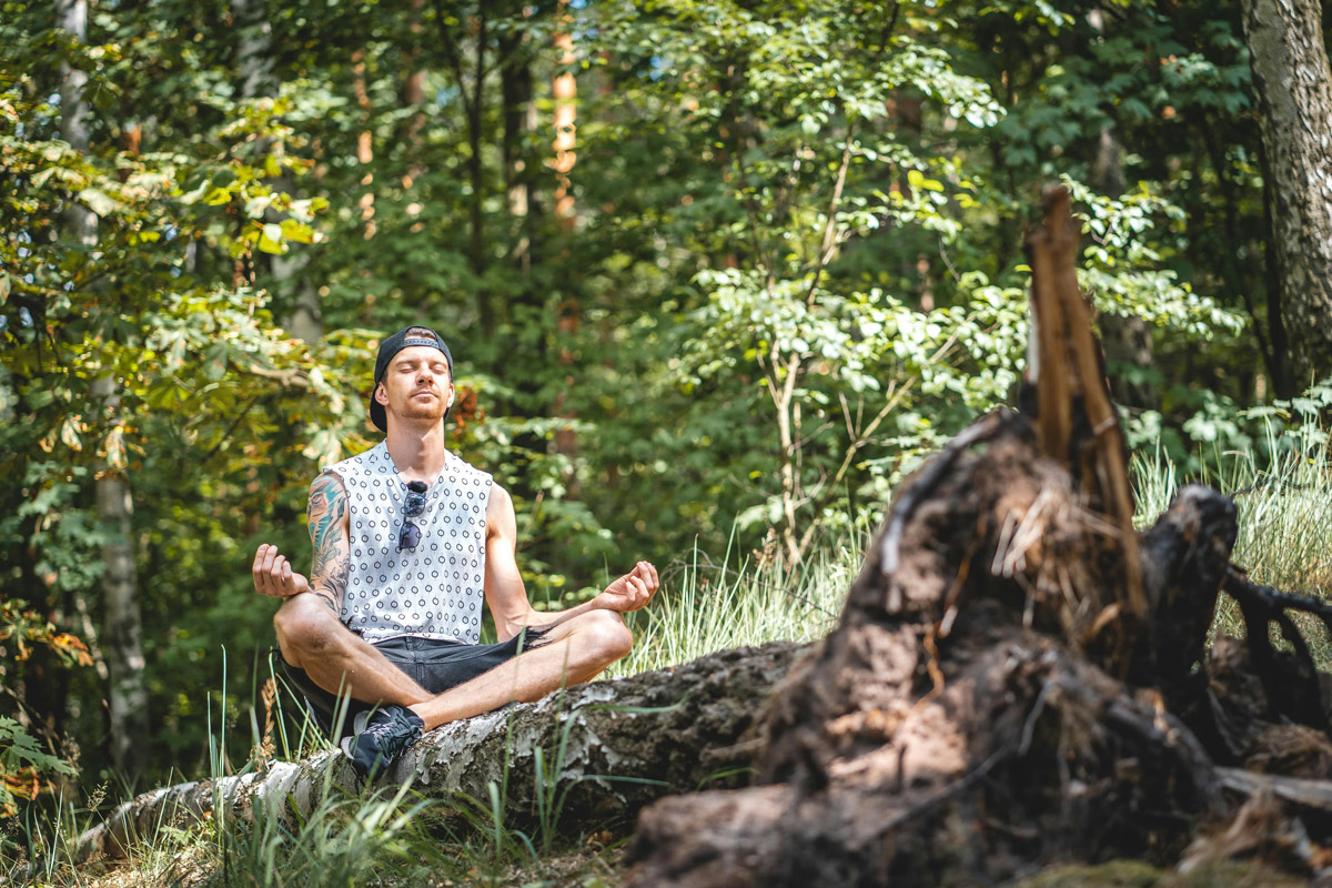 Man meditating peacefully on a log in nature during a mental health retreat.