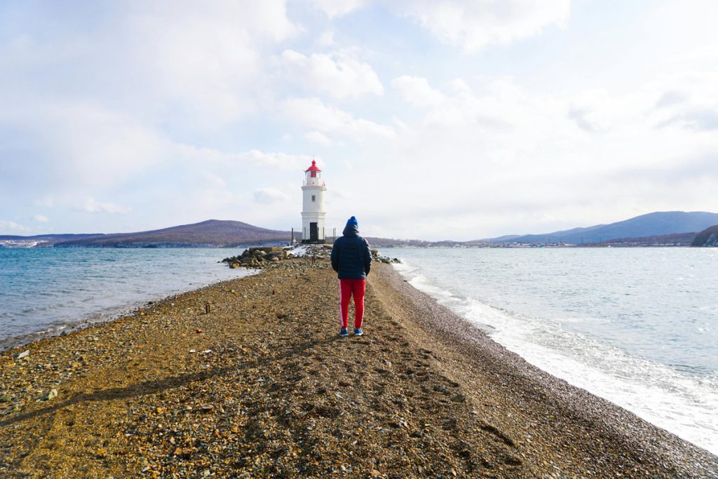 Person on a beach facing a lighthouse, symbolizing guidance and hope in the storm of anxiety.