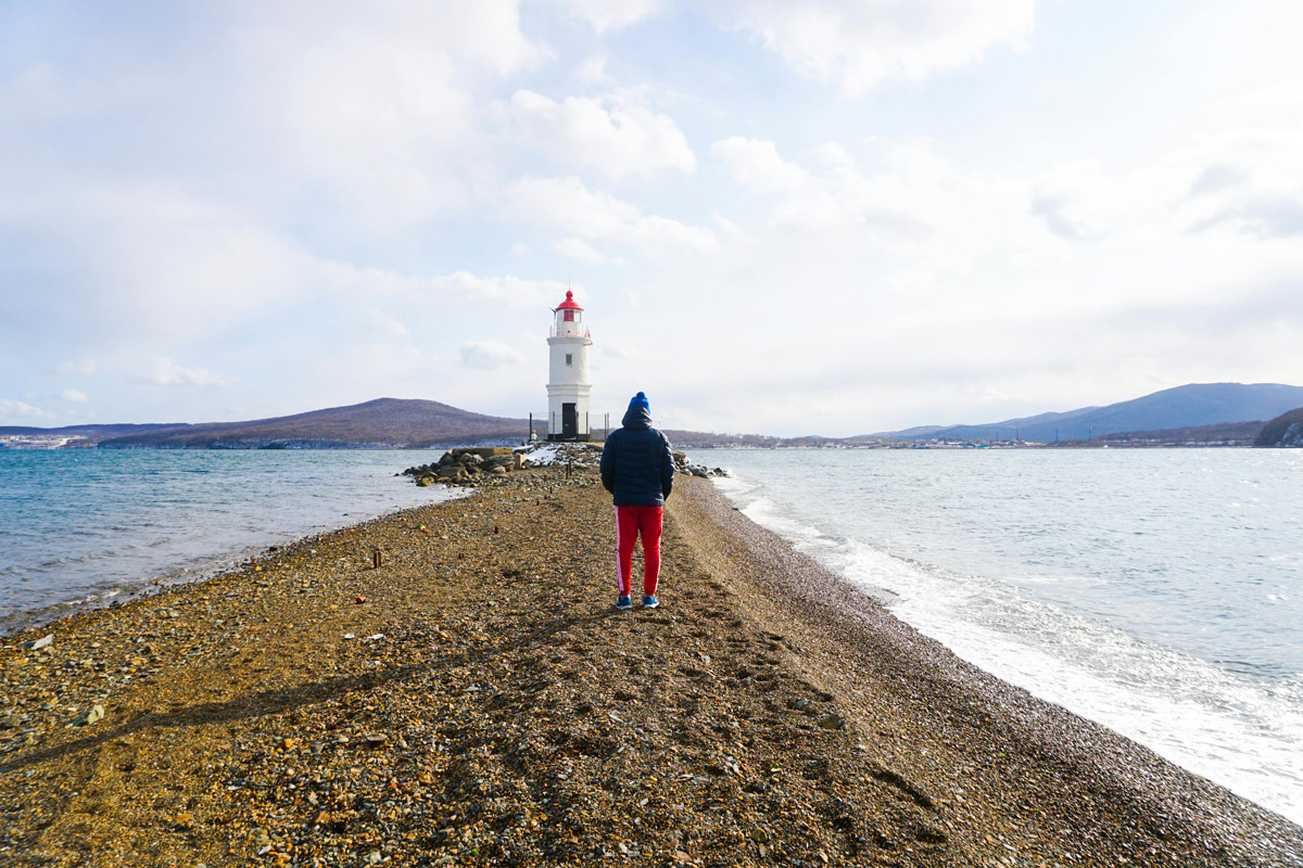 Person on a beach facing a lighthouse, symbolizing guidance and hope in the storm of anxiety.