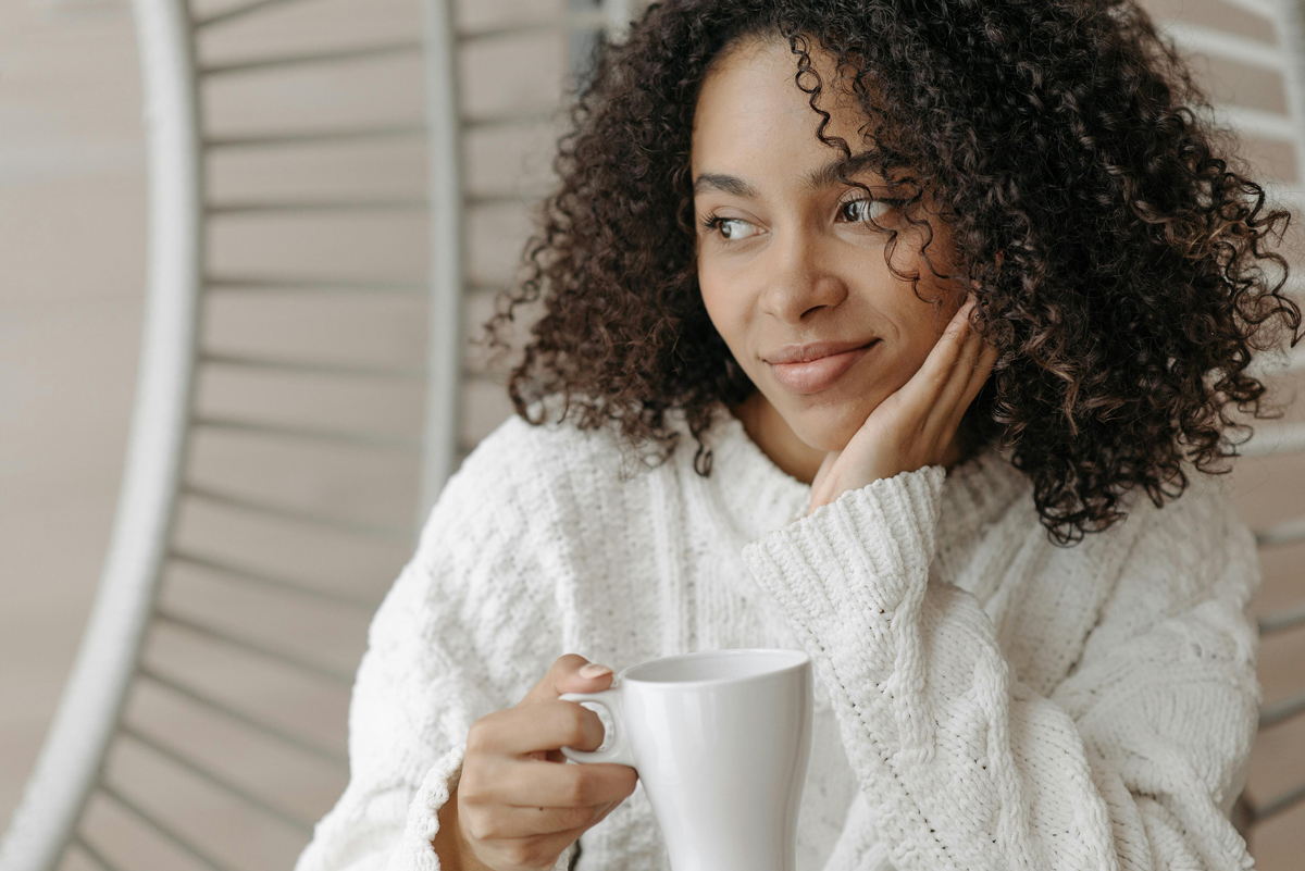 Woman with curly hair enjoying morning coffee by window, representing daily habits for emotional well-being
