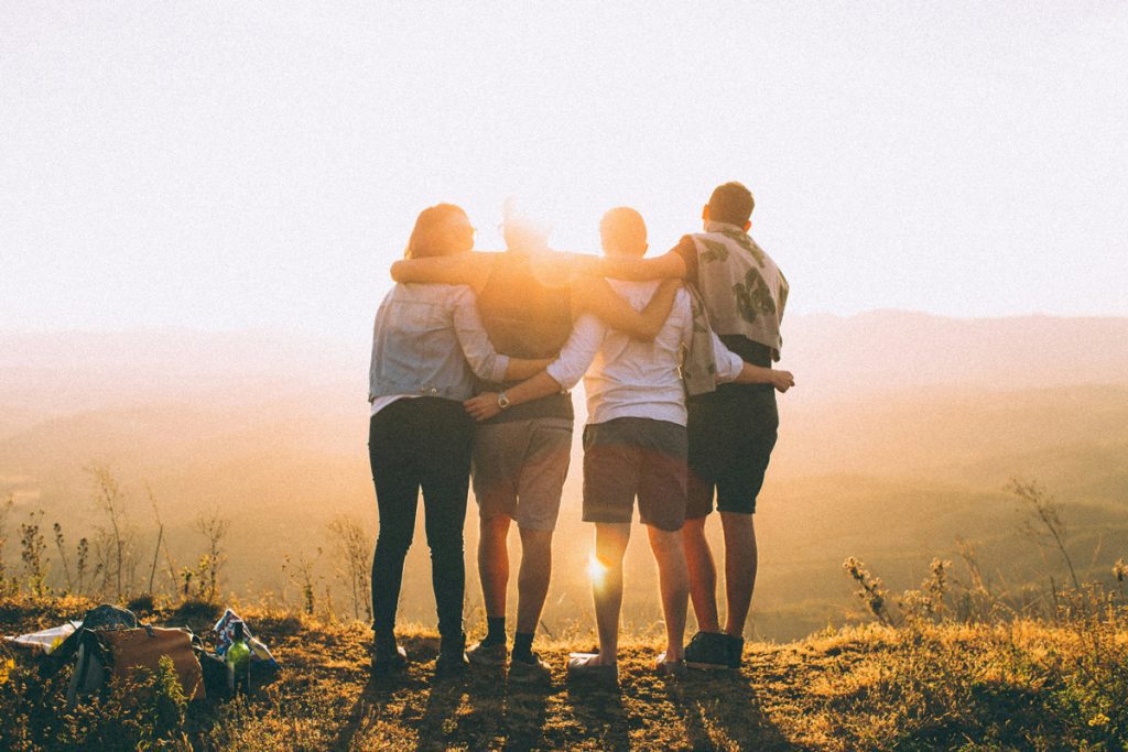 Four people standing together with arms around each other's shoulders, facing a sunset, representing family unity and support during addiction recovery after detox.