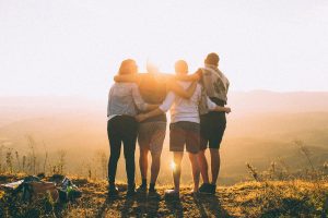 Four people standing together with arms around each other's shoulders, facing a sunset, representing family unity and support during addiction recovery after detox.