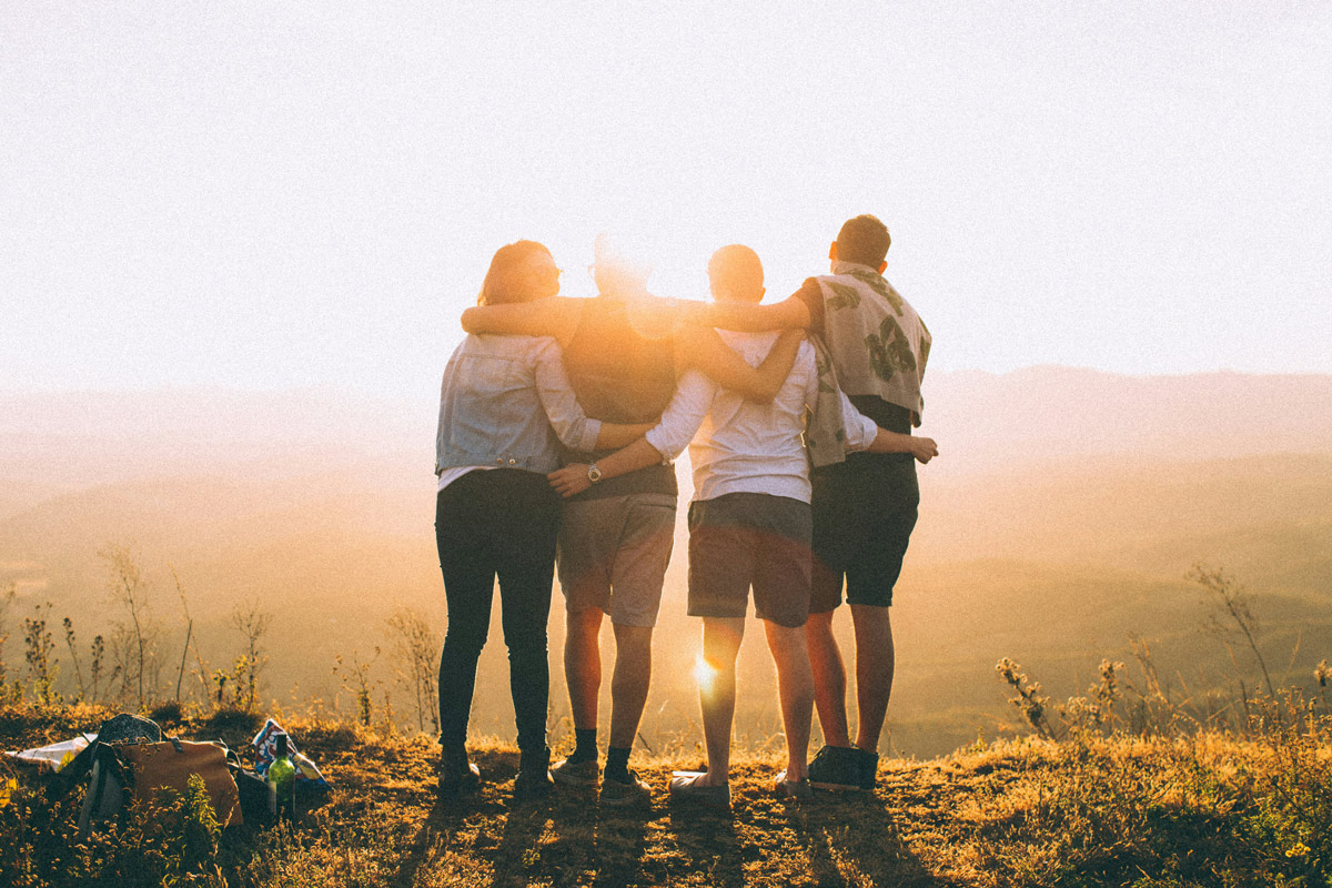 Four people standing together with arms around each other's shoulders, facing a sunset, representing family unity and support during addiction recovery after detox.