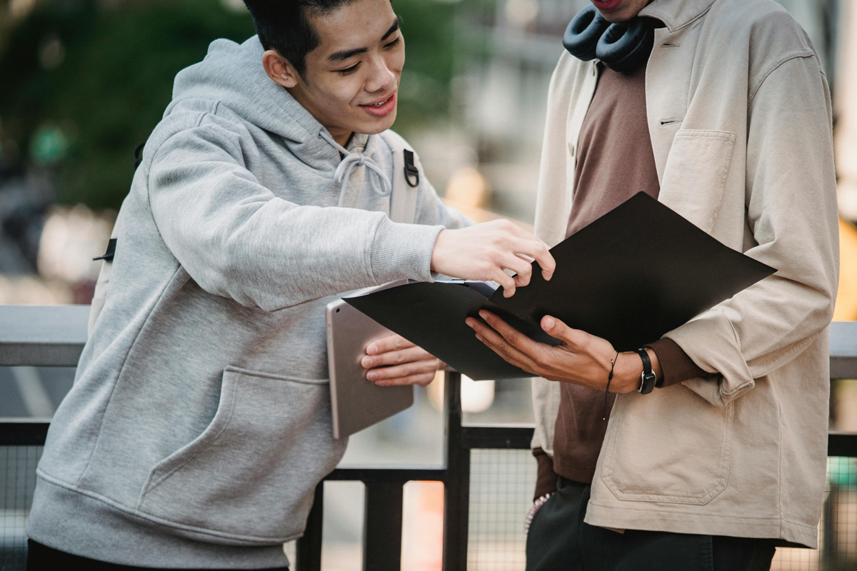 Two young men smiling and looking at documents together, representing peer support for mental health recovery