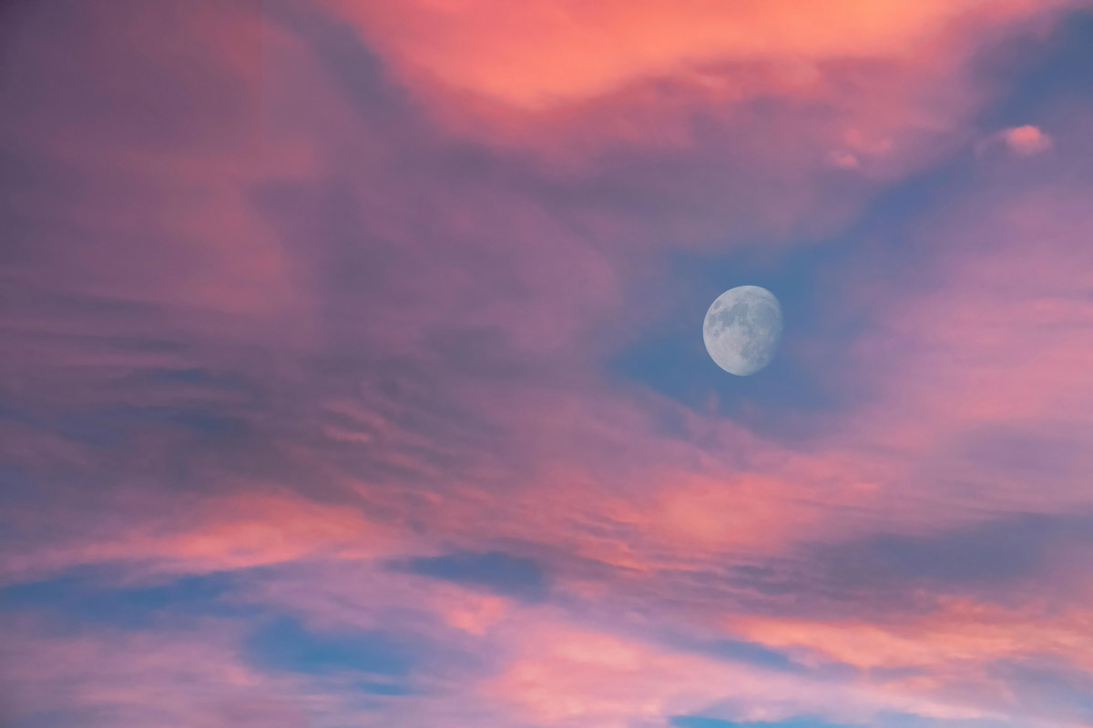 A dreamy sky with soft pink clouds and a half moon — evoking quiet and reflection