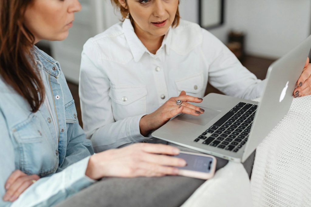 Two women sitting together reviewing mental health information on a laptop and smartphone, representing the role of technology in mental health support.
