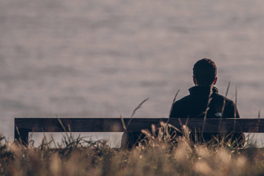Person sitting alone on a bench overlooking the water, reflecting quietly