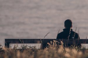 Person sitting alone on a bench overlooking the water, reflecting quietly