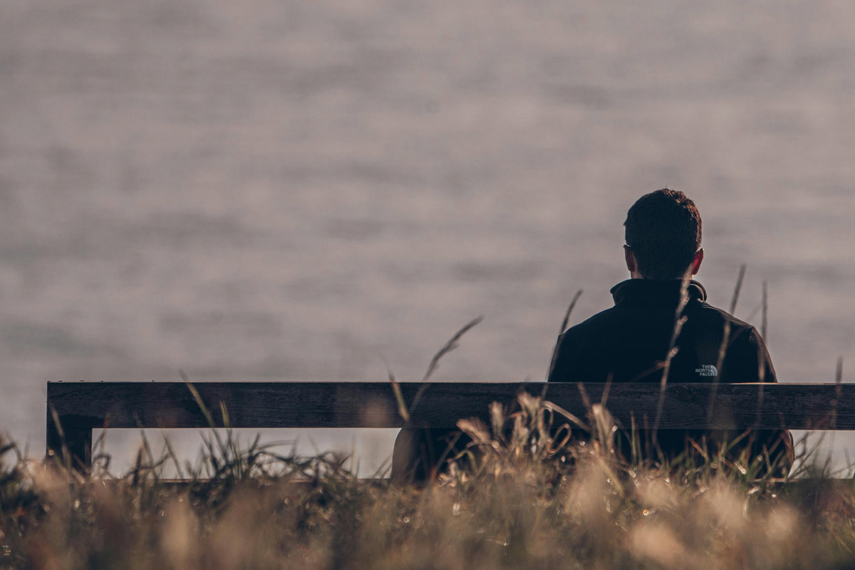 Person sitting alone on a bench overlooking the water, reflecting quietly